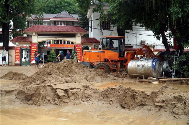Máy xúc được huy động để khơi thông dòng chảy, nạo vét bùn đất sau lũ quét tại thị trấn Mường Xén. Ảnh: TTXVN